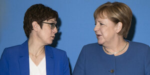 Annegret Kramp-Karrenbauer (links) neben Merkel, beide gucken sich an
