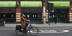 Eine Frau mit Mundschutz fährt mit ihrem fahrrad am Arbeitsamt vorbei