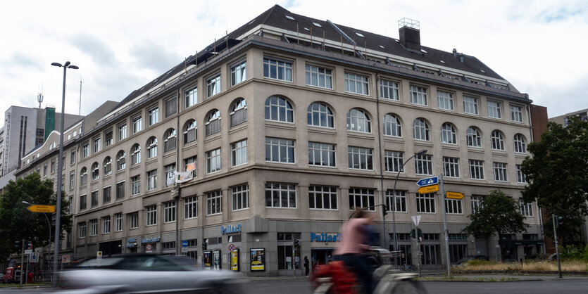 Vor dem Eckhaus an der Potsdamer Straße fährt ein Auto und eine Person auf einem Roller.