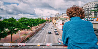 Ein Mann im blauen Pulli guckt von einer Brücke auf eine Straße