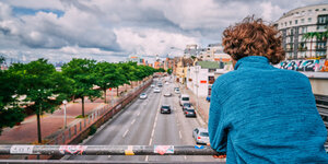 Ein Mann im blauen Pulli guckt von einer Brücke auf eine Straße