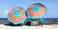 Menschen sitzen unter zwei Sonnenschirmen am Strand