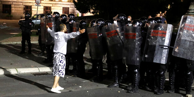 Ein Demonstrant steht allein vor einer schwer bewaffneten Polizeikette