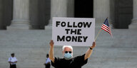 Ein Mann mit Mundschitz und US-Flagge hält ein Plakat mit der Aufschrift: Follow the money.