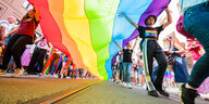 Eine große Regenbogenflagge wird von Menschen getragen