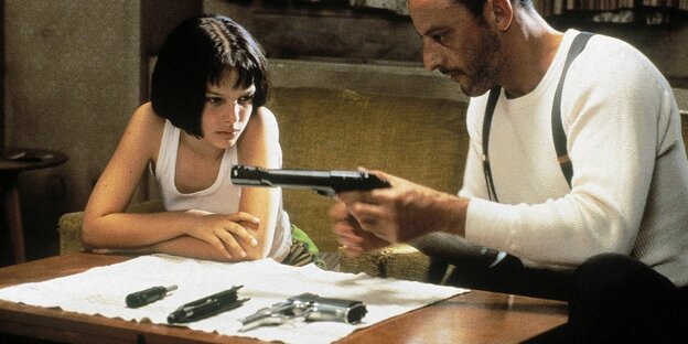 Ein Schauspieler zeigt einer jüngeren Schauspielerin eine Pistole.
