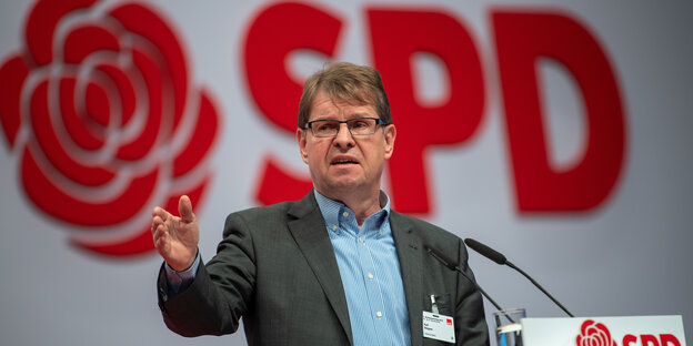 Ein Mann hinter einem MIkrofon hebt die hand, dahinter der Schriftzug SPD und eine stilisierte Rose