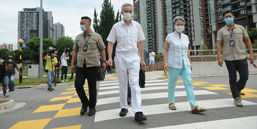 Singapurs Ministerpräsident Lee Hsien Loong und seine Frau Ho Ching mit zwei Begleitern überqueren eine Straße auf einem Zebrastreifen vor der Kulisse der Hochhäuser von Singapur