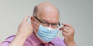 Bundeswrtschaftminister Peter Altmaier im pinken Hemd legt sich einen Mund-und-Nasenschutz an