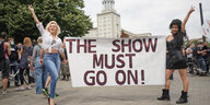 Zwei Darstellerinnen aus dem Estrel-Hotel halten bei einer Demonstration der Veranstaltungsbranche ein Plakat mit der Aufschrift "The Show must go on!
