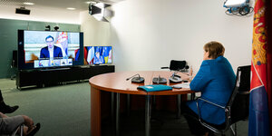 Angela Merkel sitzt an einem Tisch und schaut auf einen Bildschirm, der Vucic zeigt.