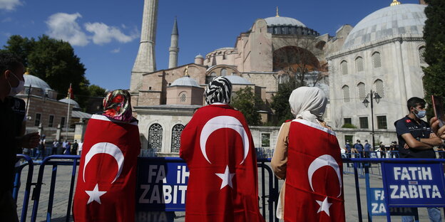 Drei in die türkische Nationalfahne gehüllt Frauen mit Kopftuch stehen vor der Hagia Sofia. Das Museum wird wieder eine Moschee