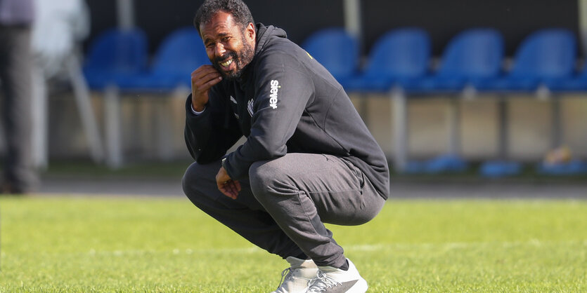 Ein Mann in Sportkleidung hockt auf einem Fußballrasen