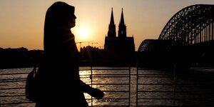 Eine Spaziergängerin mit Kopftuch spaziert am Rheinboulevard in Köln entlang