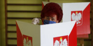 Frau mit Mundschutz in einer Wahlkabine mit polnischem Wappen