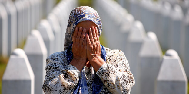 Eine Frau mit Kopftuch steht auf muslimischem Friedhof und hält ihre Hände vor ihr Gesicht.