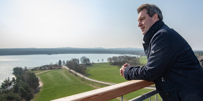 Söder auf ein Geländer gelehnt blickt auf ein Gewässr