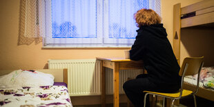 Eine Frau sitz an einem Tisch und schaut aus einem Fenster.