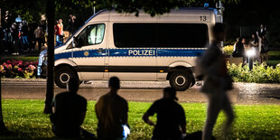 Im Vordergrund Schattenumrisse von Menschen, im Hintergrund ein Polizeifahrzeug.