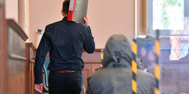 Zwei Personen verdecken ihr Gesicht in einem Gerichtssaal.