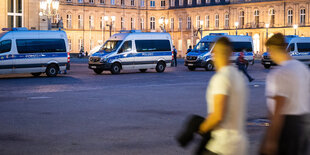 Im Vordergrund unscharfe Personen, im Hintergrund Polizeifahrzeuge vor einem Schloss.