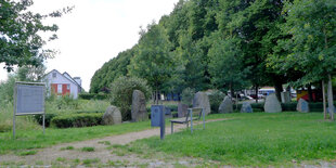 Halbrund aus aufgerichteten Natursteienen mit Inschriften, davor eine Sitzbank dahinter eine Baumreihe