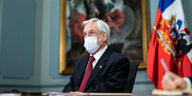Chiles Präsident sitzt mit Maske an einem Schreibtisch, hinter ihm die Nationalfahne