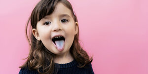 Kind vor pinkem Hintergrund streckt die Zunge heraus.