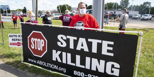 Menschen mit Atemschutzmasken halten ein Transparent auf dem steht "Stop State killing"
