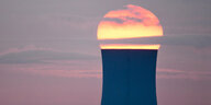 Ein Kühlturm eines Kraftwerkes mit der aufgehenden Sonne dahinter.
