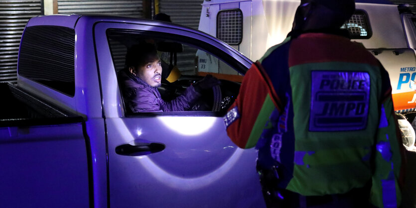 Ein Polizist leuchtet mit einer Taschenlampe in ein Auto.