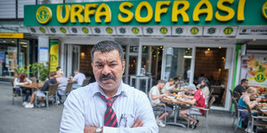 Ein Mann mit verschränkten Armen und wütendem Blick steht vor einem Restaurant