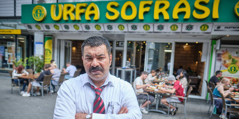 Ein Mann mit verschränkten Armen und wütendem Blick steht vor einem Restaurant