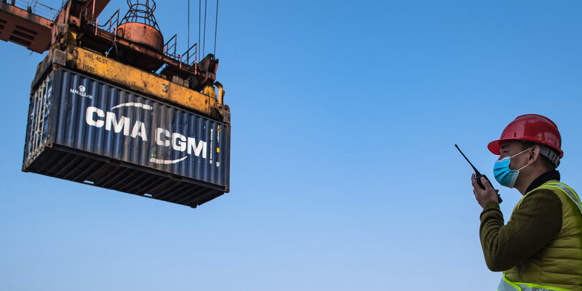 Ein Hafenarbeiter miT Funkgerät vor einem Container.