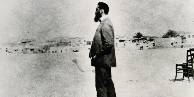 Krisselige Schwarz-Weiß-Aufnahmen eines Mannes mit Bart und Torpenhelm im Profil, der vo einer Siedlung steht