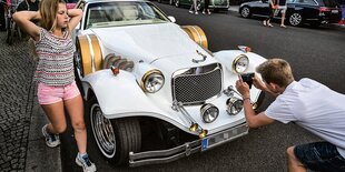 Mädchen räkelt sich vor Oldtimer, Junge fotografiert