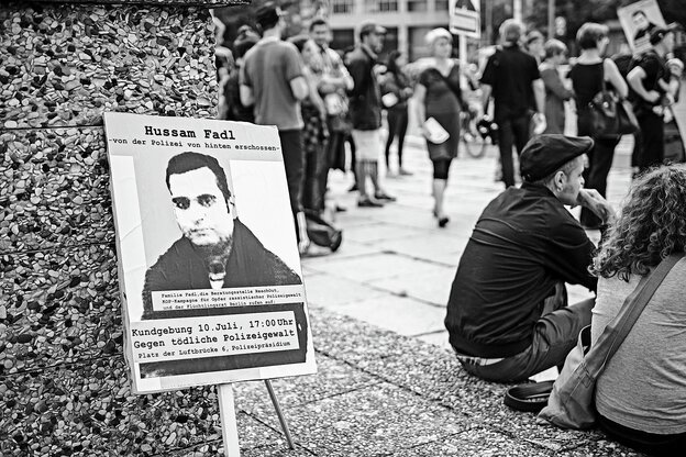 Ein Plakat mit Hussam Fadl Portrait, dahinter eine Kundgebung gegen tödliche Polizeigewalt