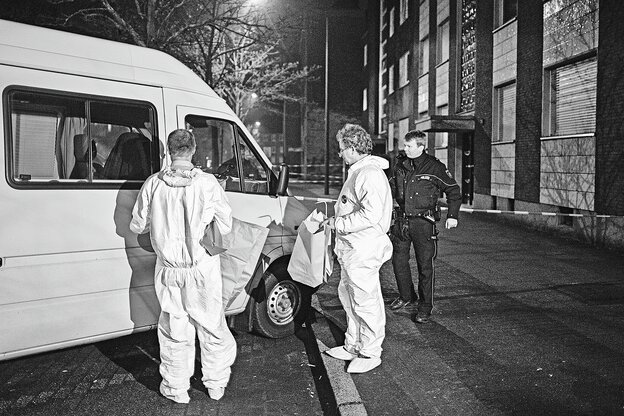 Zwei Männer in weißen Anzügen und ein Polizist stehen vor einem abgesperrten Haus Zwei Männer in weißen Anzügen und ein Polizist stehen vor einem abgesperrten Haus