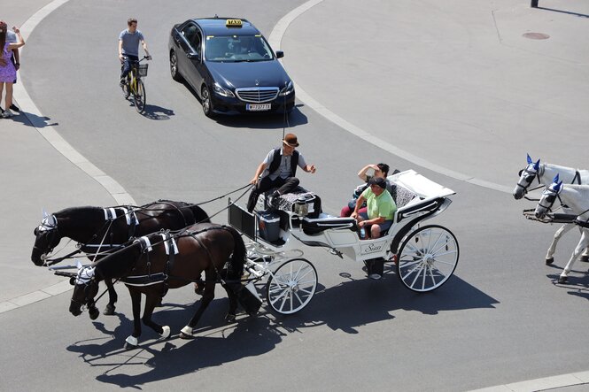 Kutschenun, Radfahrer, FußgängerInnen und ein Taxi auf einem Platz.