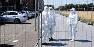 Menschen in Schutzanzügen hinter einem Zaun.