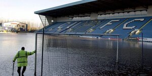 Mensch in Warnweste blickt auf überflutetes Fußballstadion