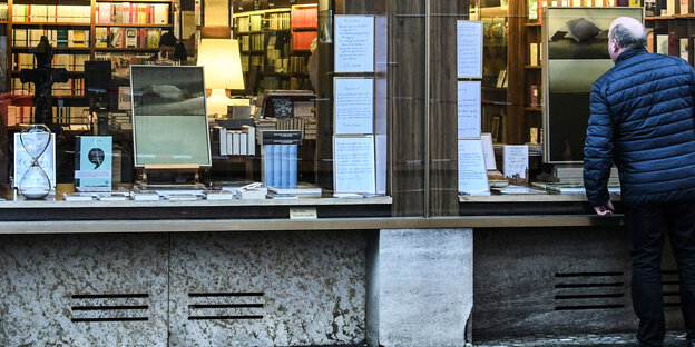 Ein Mann in Rückenansicht schaut in das Fenster eines Buchladens.