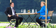 Merkel und Conte sitzen an einem Tisch unterm Sonnenschirm