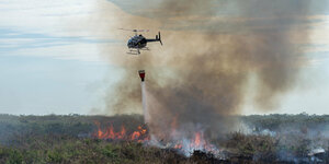 Ein Hubschrauber schüttet Wasser auf einen brennenden Wald