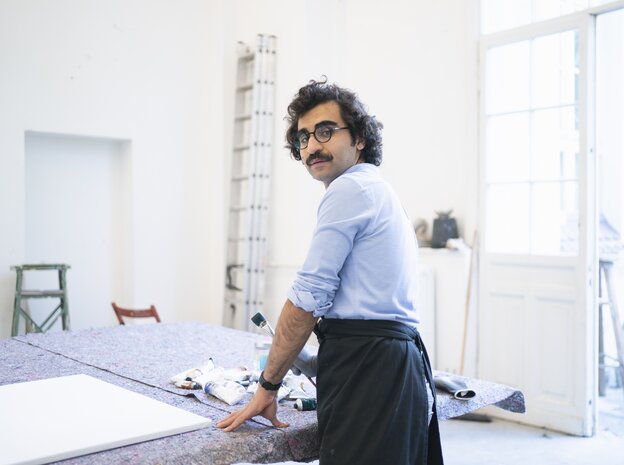 Kunststudent Ali Yass steht in seinem Atelier und guckt in die Kamera Kunststudent Ali Yass steht in seinem Atelier und guckt in die Kamera