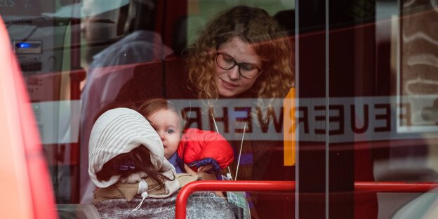 Eine Frau mit Locken beugt sich zu einer Frau, die ein Kind im Arm hält Eine Frau mit Locken beugt sich zu einer Frau, die ein Kind im Arm hält