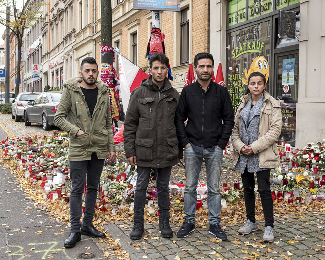 3 MÄnner und eine Frau stehen vor einem Blumengedenken vor dem Imbissladen