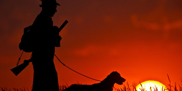 Dunkle Sllhouette eines Jägers und seines Hundes vor einem Sonnenuntergang