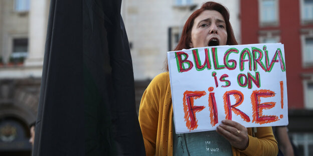 Eine Frau hält ein Plakat in die Höhe. Darauf steht: Bulgarien brennt!