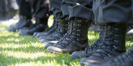 Mehrere Militärstiefel und der untere Saum von Militärhosen. Die Stiefel stehen in einer Reihe auf grünem Rasen